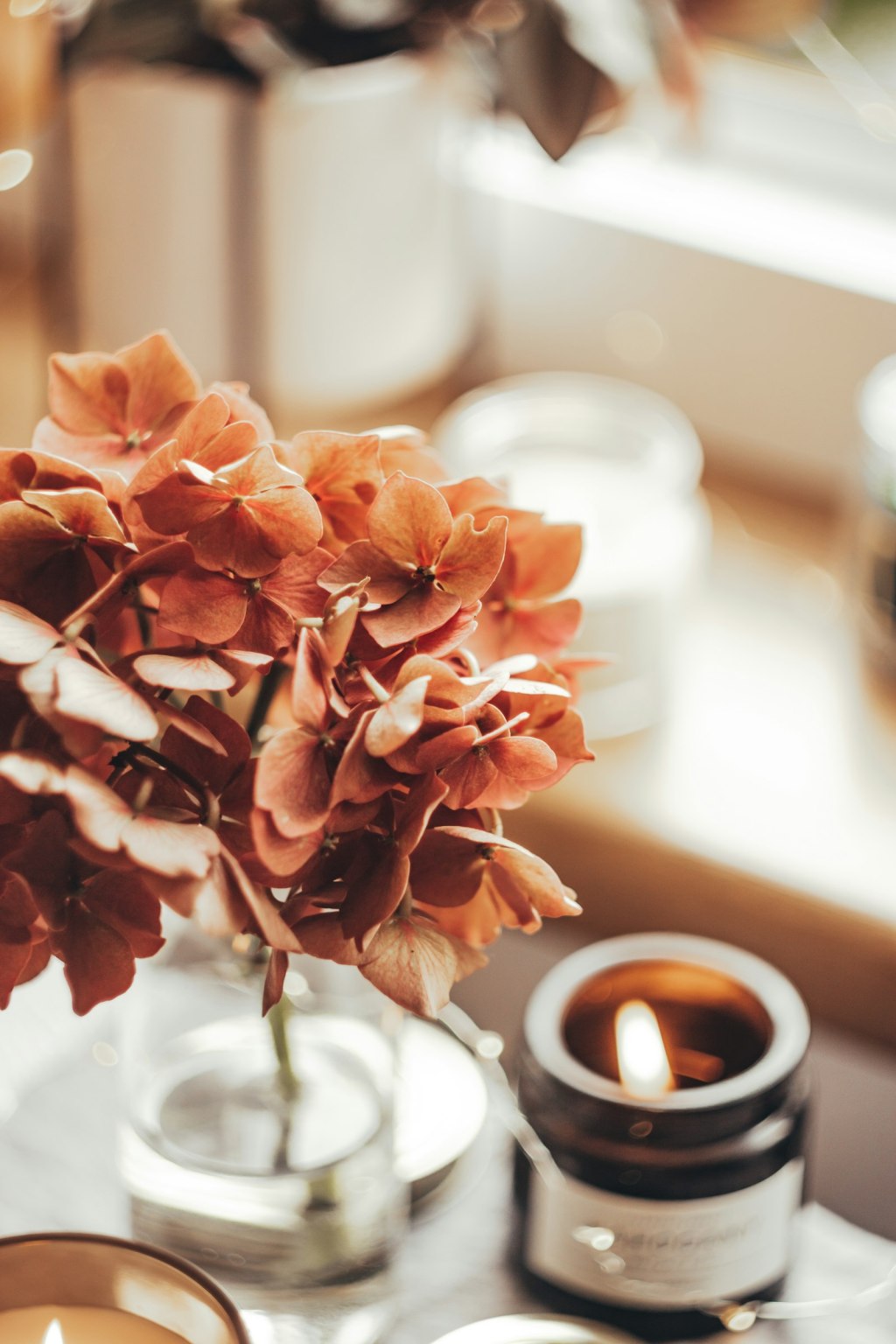 A lit candle beside a small bunch of spring flowers on a table, set up for a Beltane flower and ribbon spell
