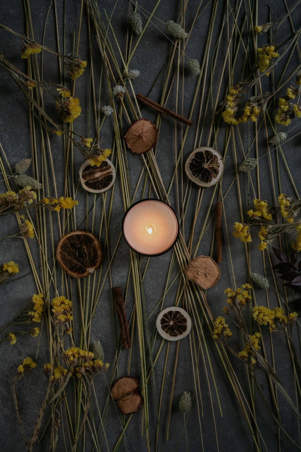 A lit candle surrounded by dried flowers and herbs, the ingredients used when dressing a spell candle