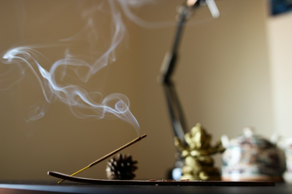 A lit stick of incense with a thin curl of smoke rising in low, moody light